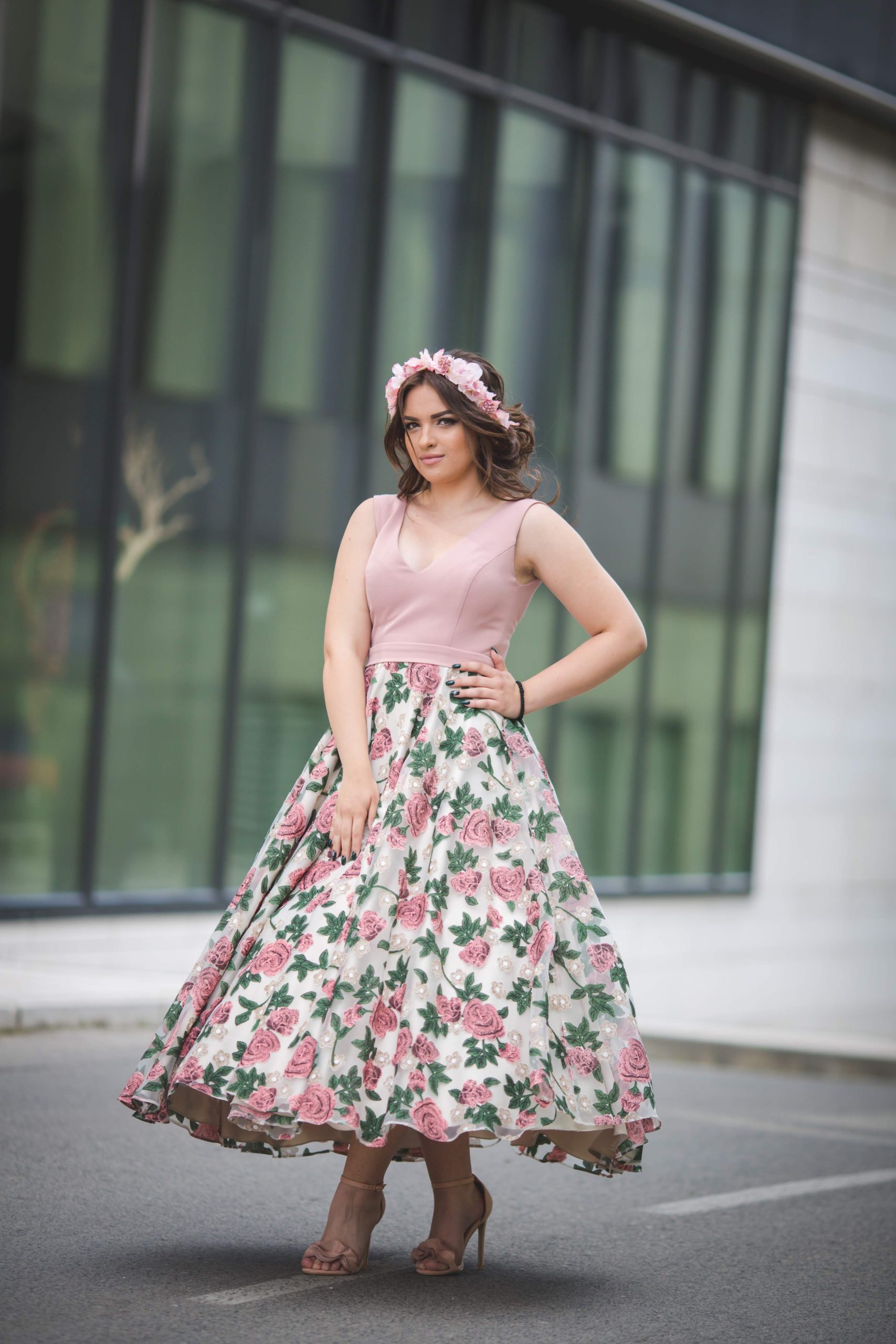 A Caucasian standing in front of a modern building in a pink dress and hairband