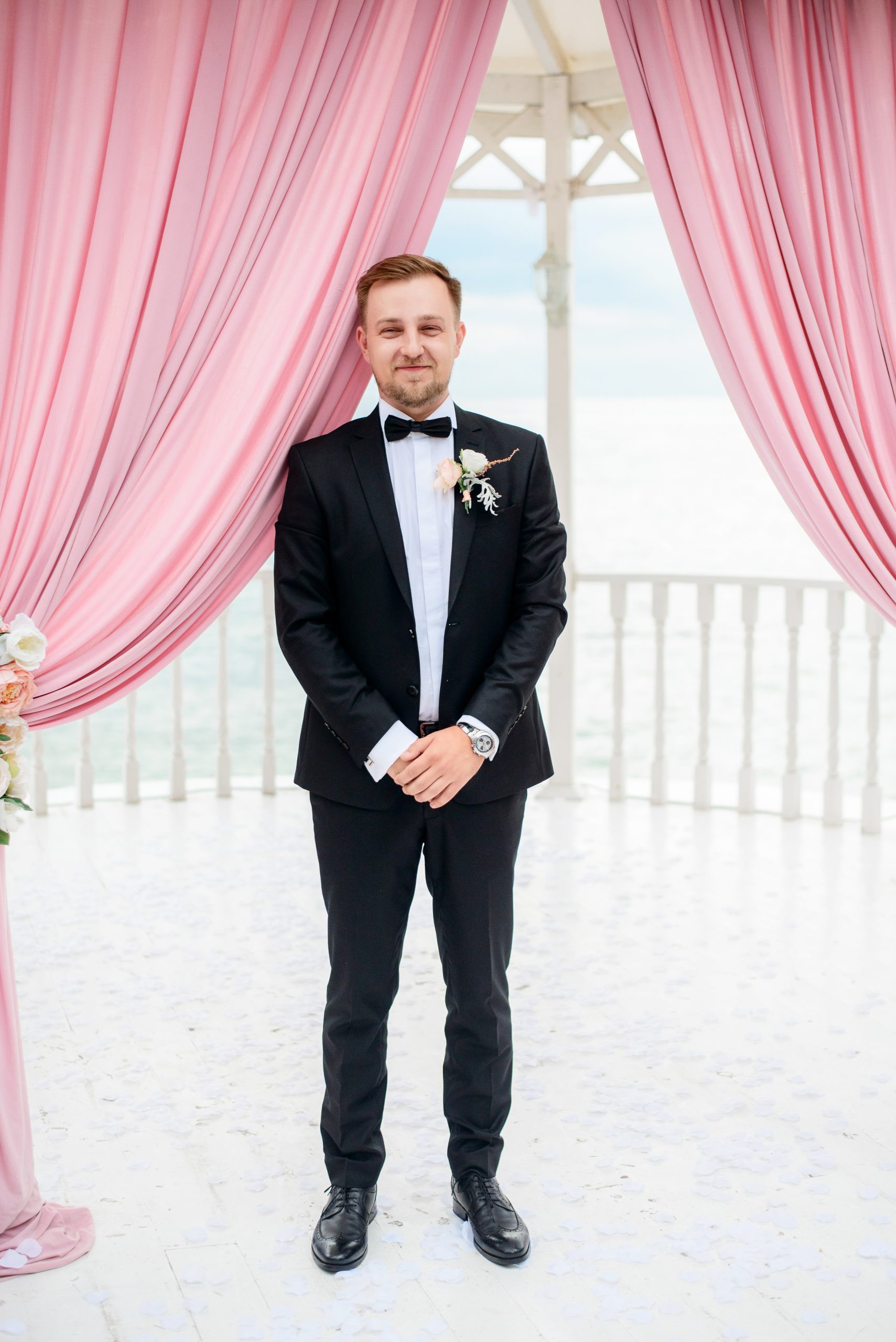 Groom stands alone under the tent for wedding ceremony by the sea